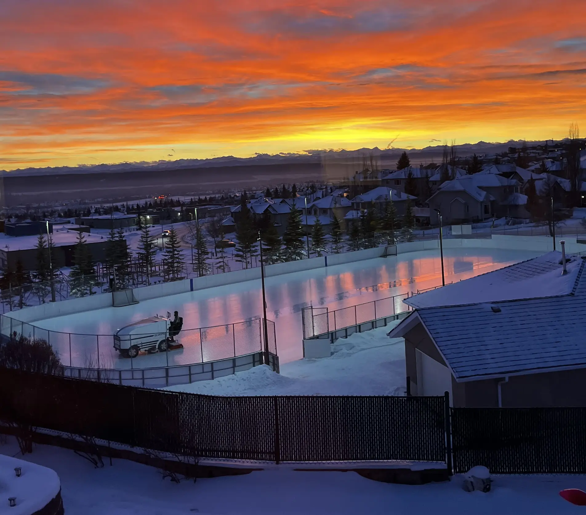 The Signal Hill outdoor rink at sunset, winter sky pink and orange over the boards and Rocky Mountain skyline.