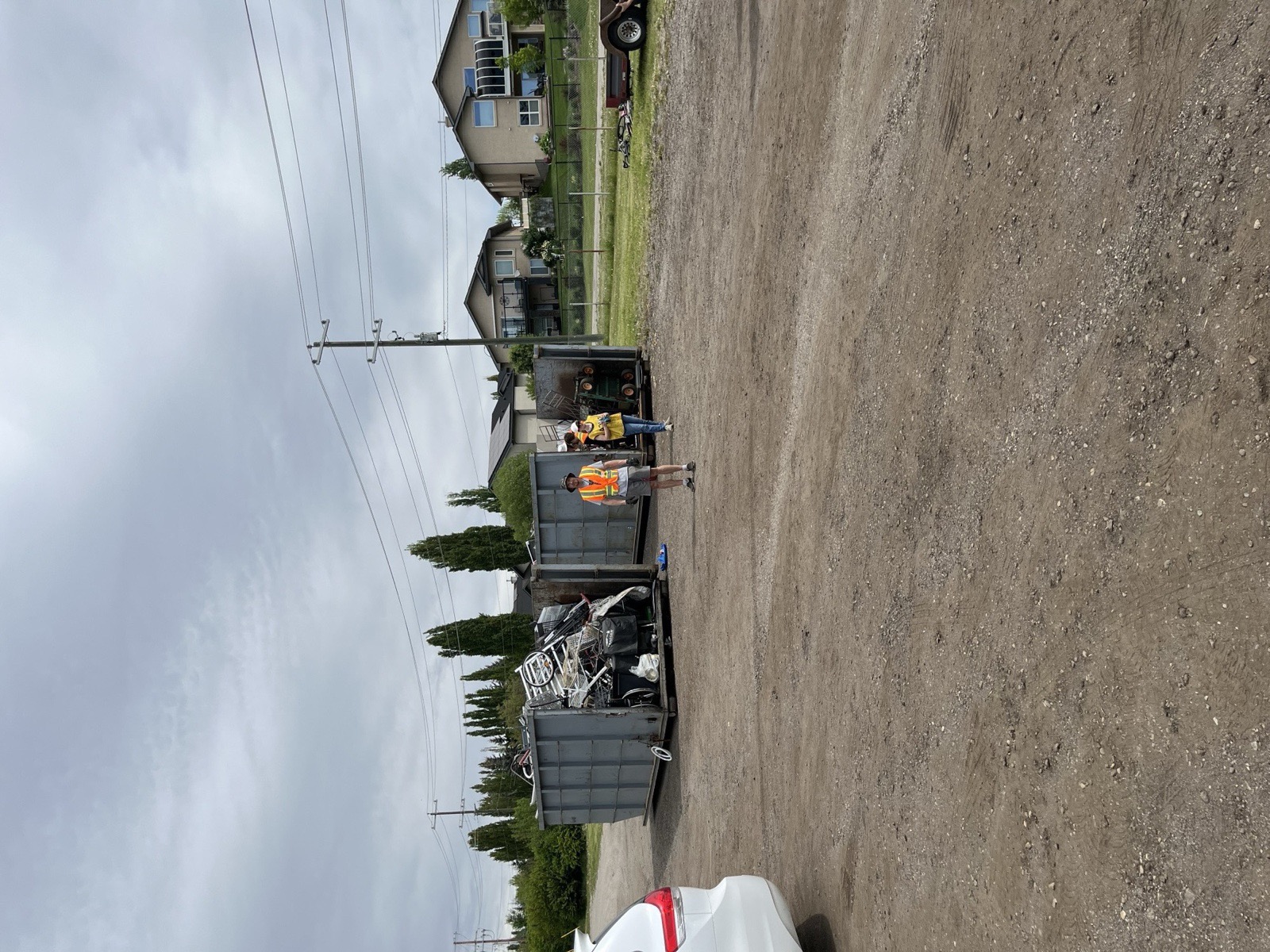 A metal recycling dumpster half-full of household items; a volunteer in a high-vis vest beside it.