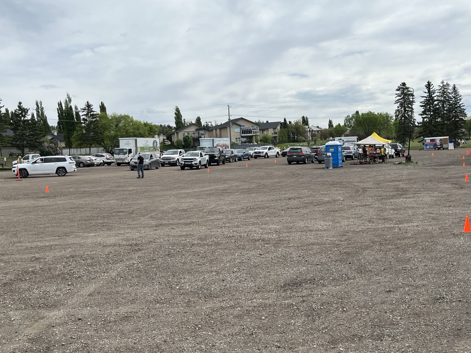 Wide view of the full cleanup site, parked cars, tents, vendor booths, a porta-potty, and the queue.