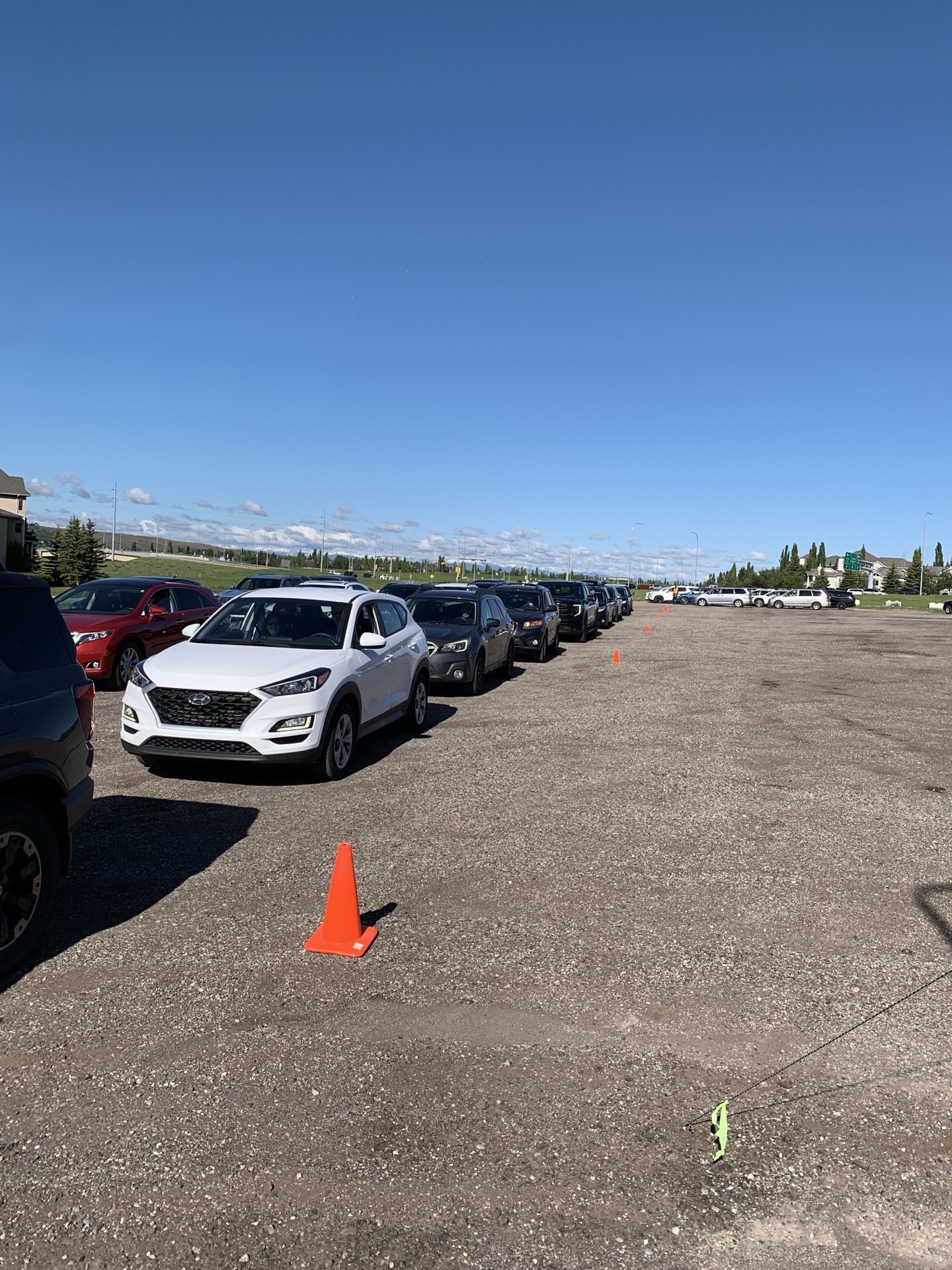 A long queue of cars down the lane — a Hyundai at the front, traffic cone marking the pinch point, blue sky.