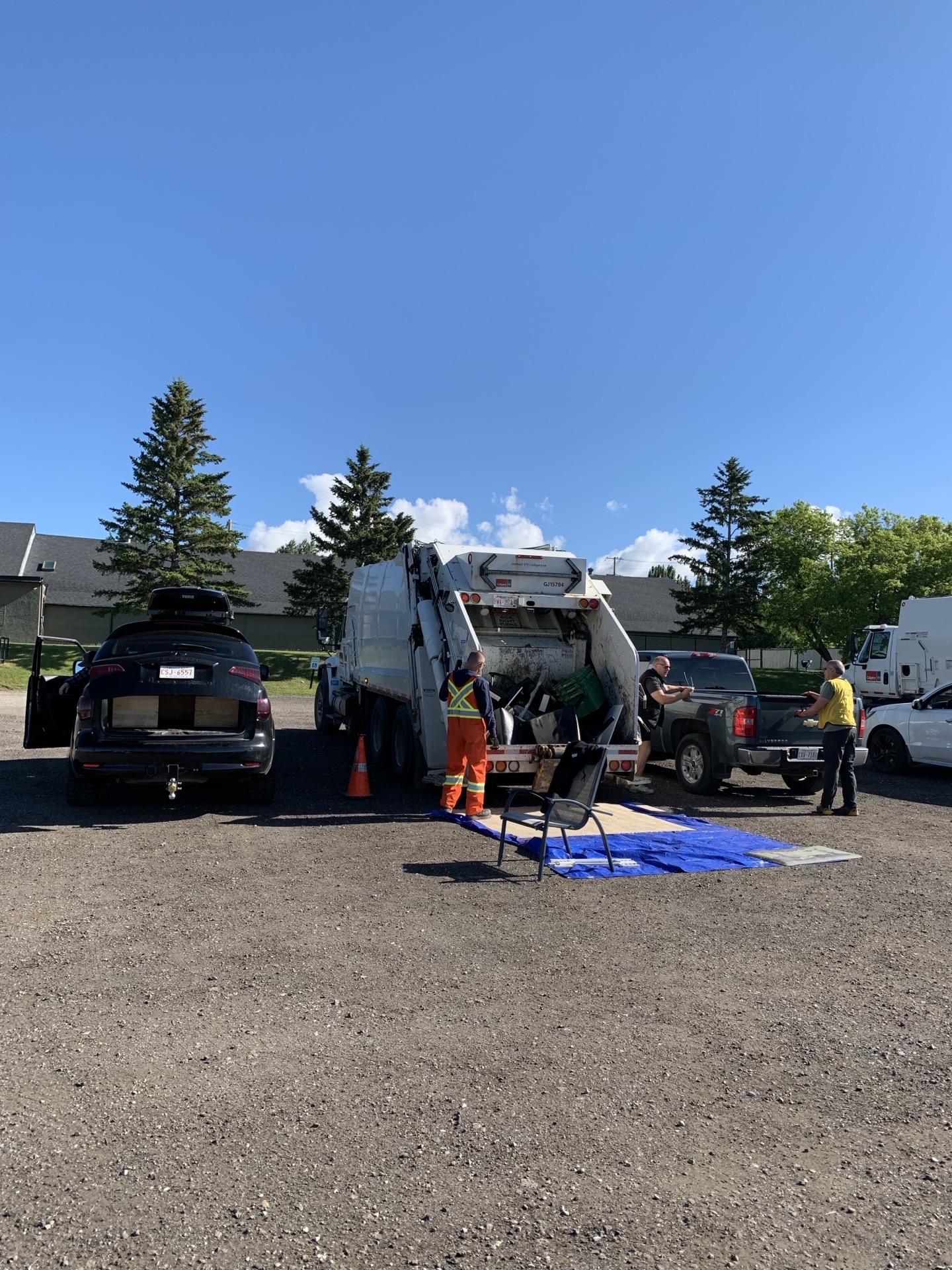 Truck loading in progress — orange-coveralls City worker, chair pulled up, blue tarp on the ground.