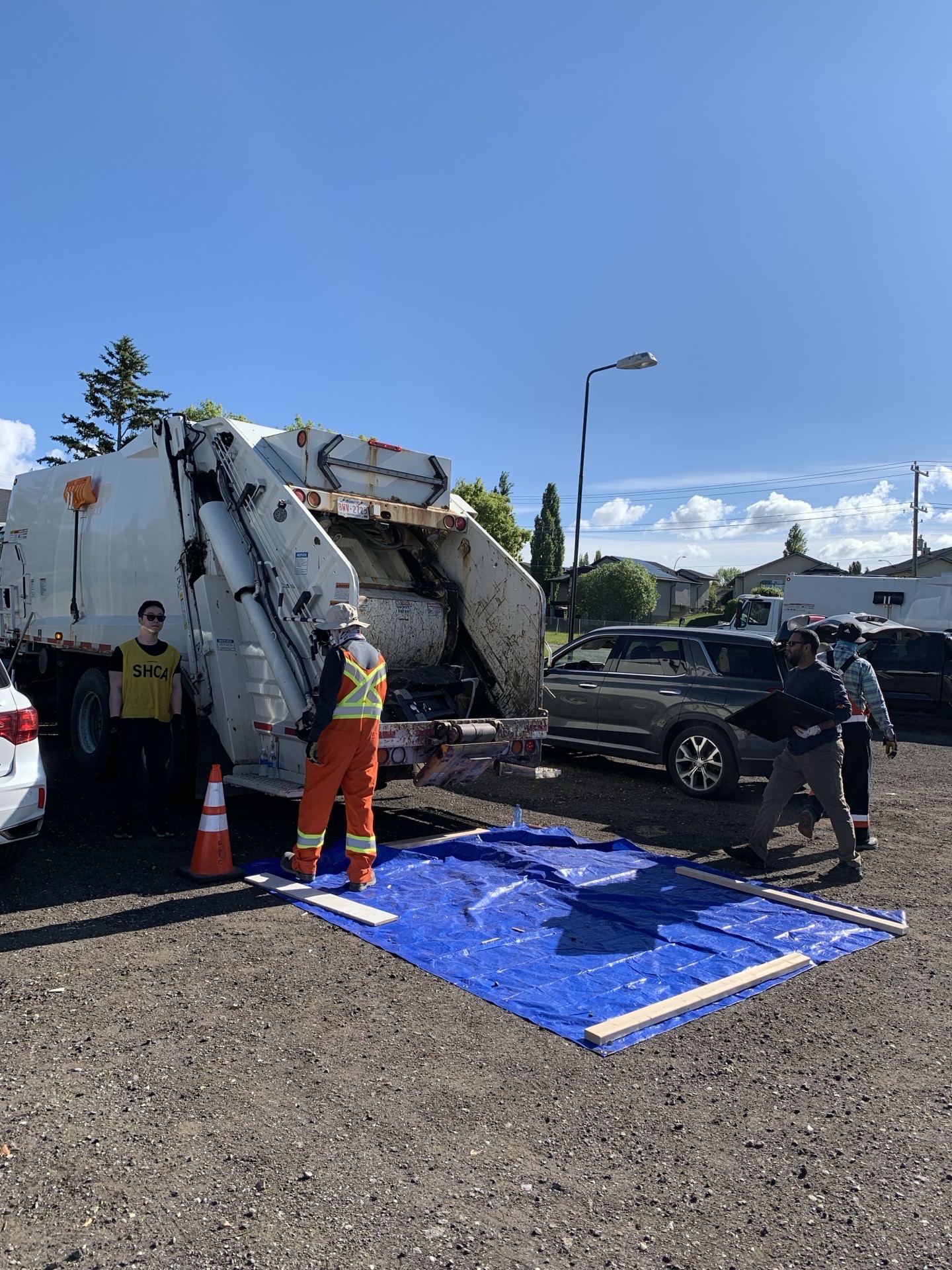 A City garbage truck being loaded — volunteer in orange coveralls directing traffic, donation tarp on the ground.