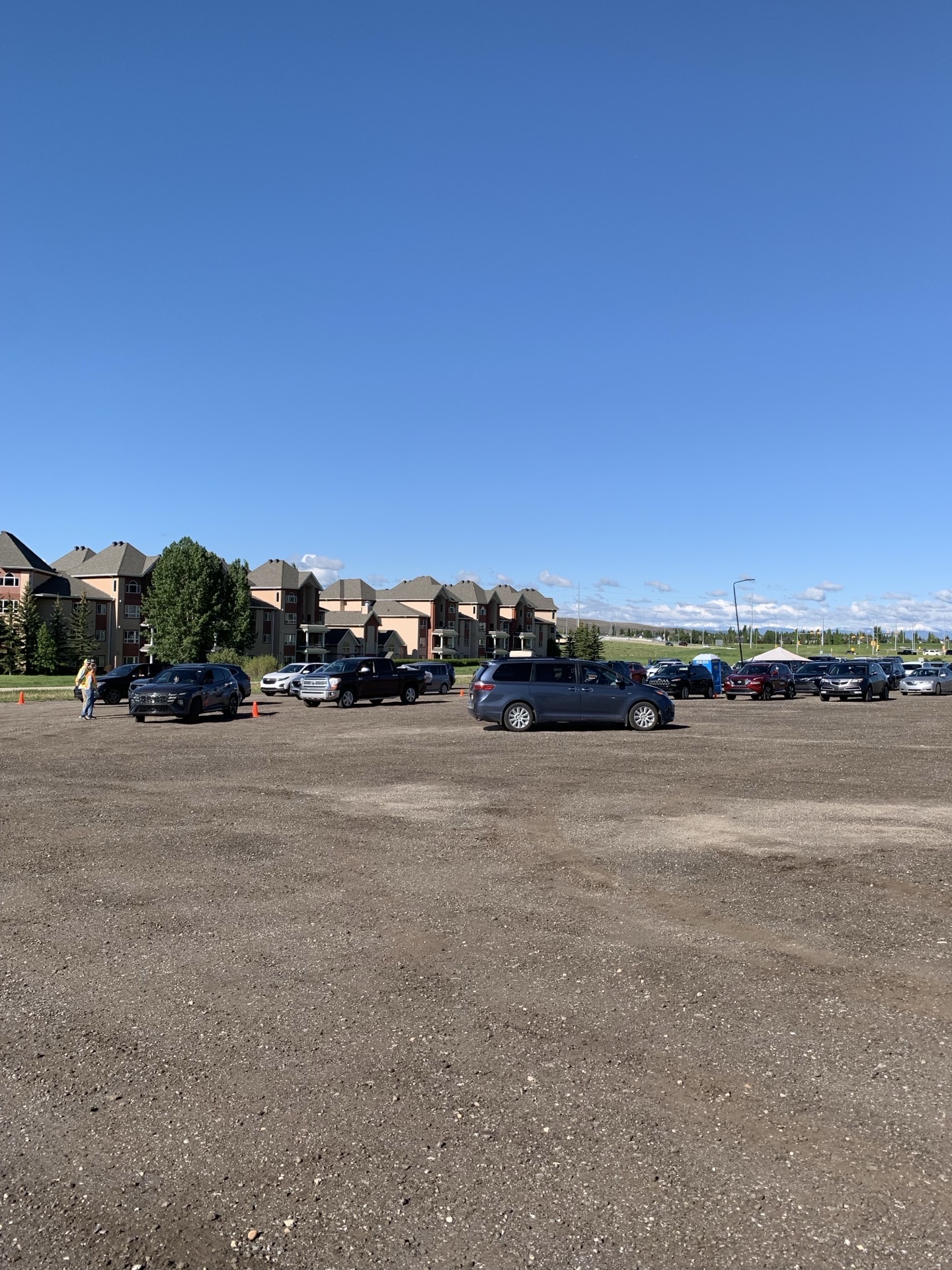 Wide-angle of the staging lot mid-morning, cars trickling in, no line yet, big blue sky overhead.