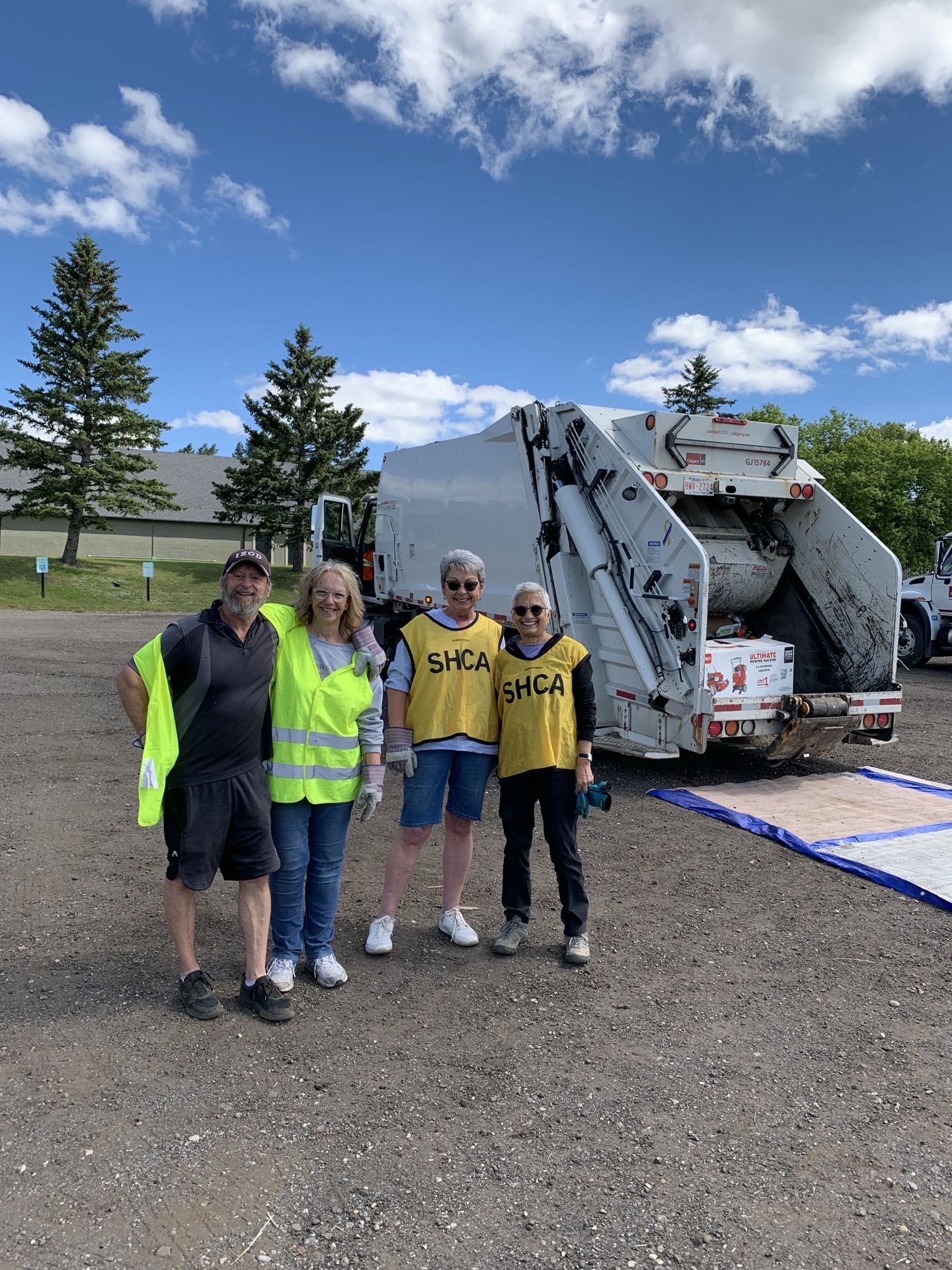 Four SHCA volunteers in safety vests posed with a garbage truck behind them, blue sky.
