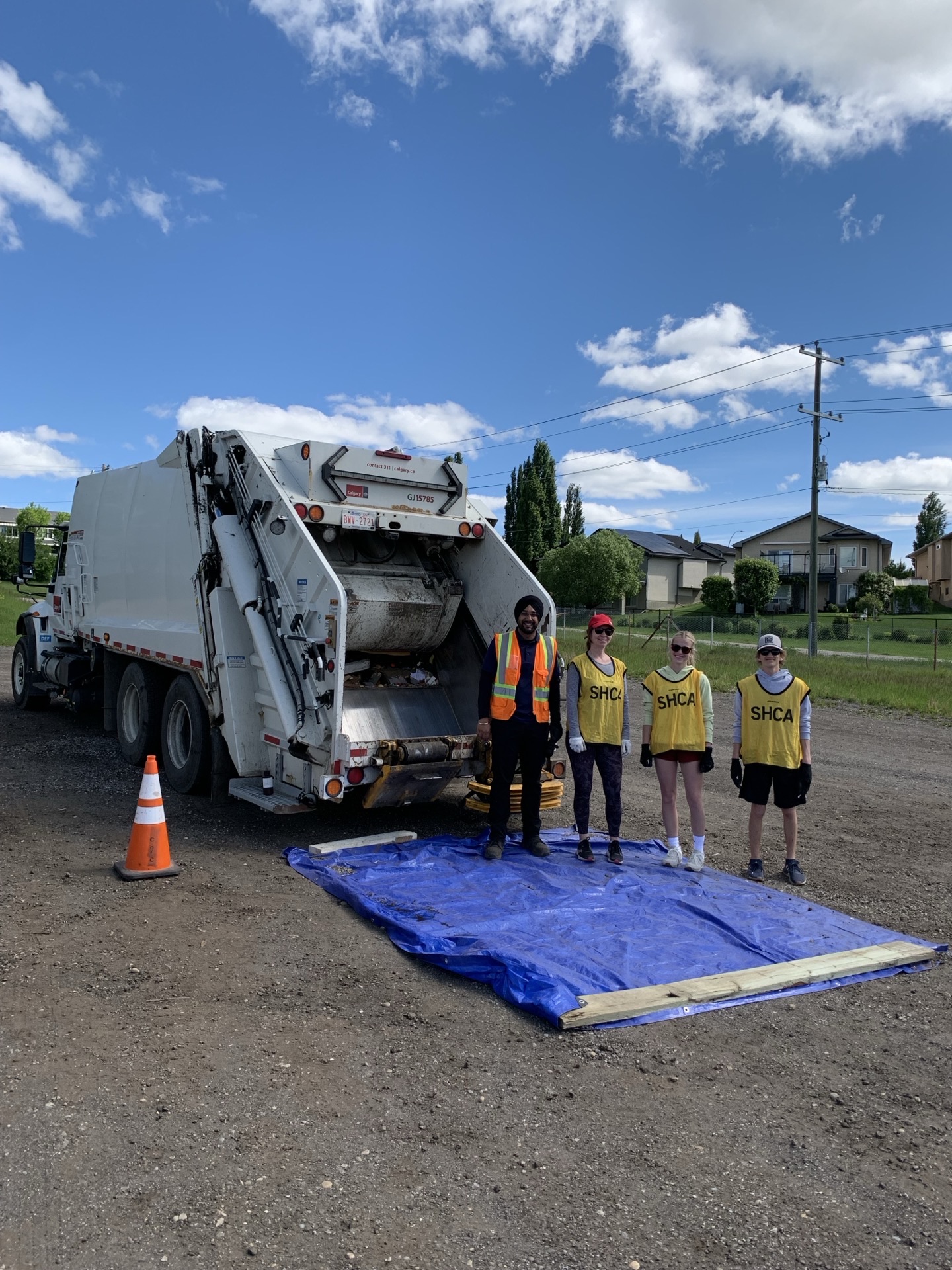 Four SHCA-vested volunteers lined up in front of the garbage truck, blue tarp on the ground.
