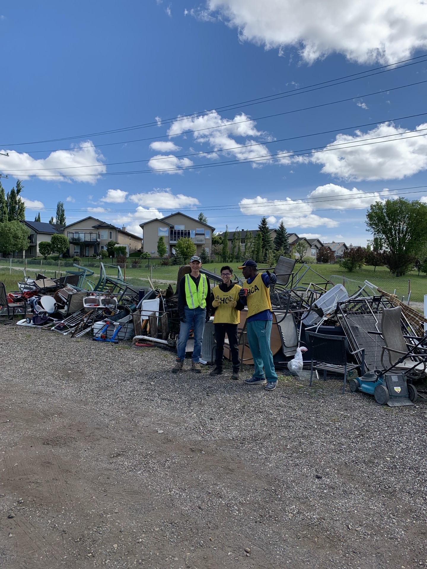 Three volunteers standing in front of a long line of dropped-off household items waiting to be loaded into trucks.