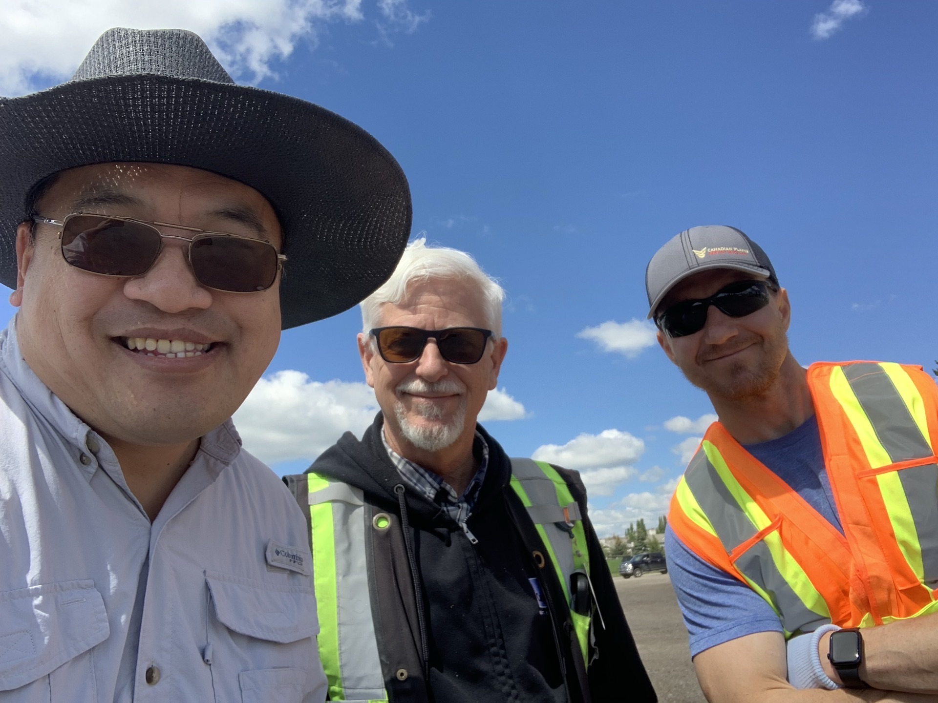 Close-up of the three cleanup organizers — Behrokh, Kiel in the wide-brimmed hat, and Rob — bright sun and blue sky behind.