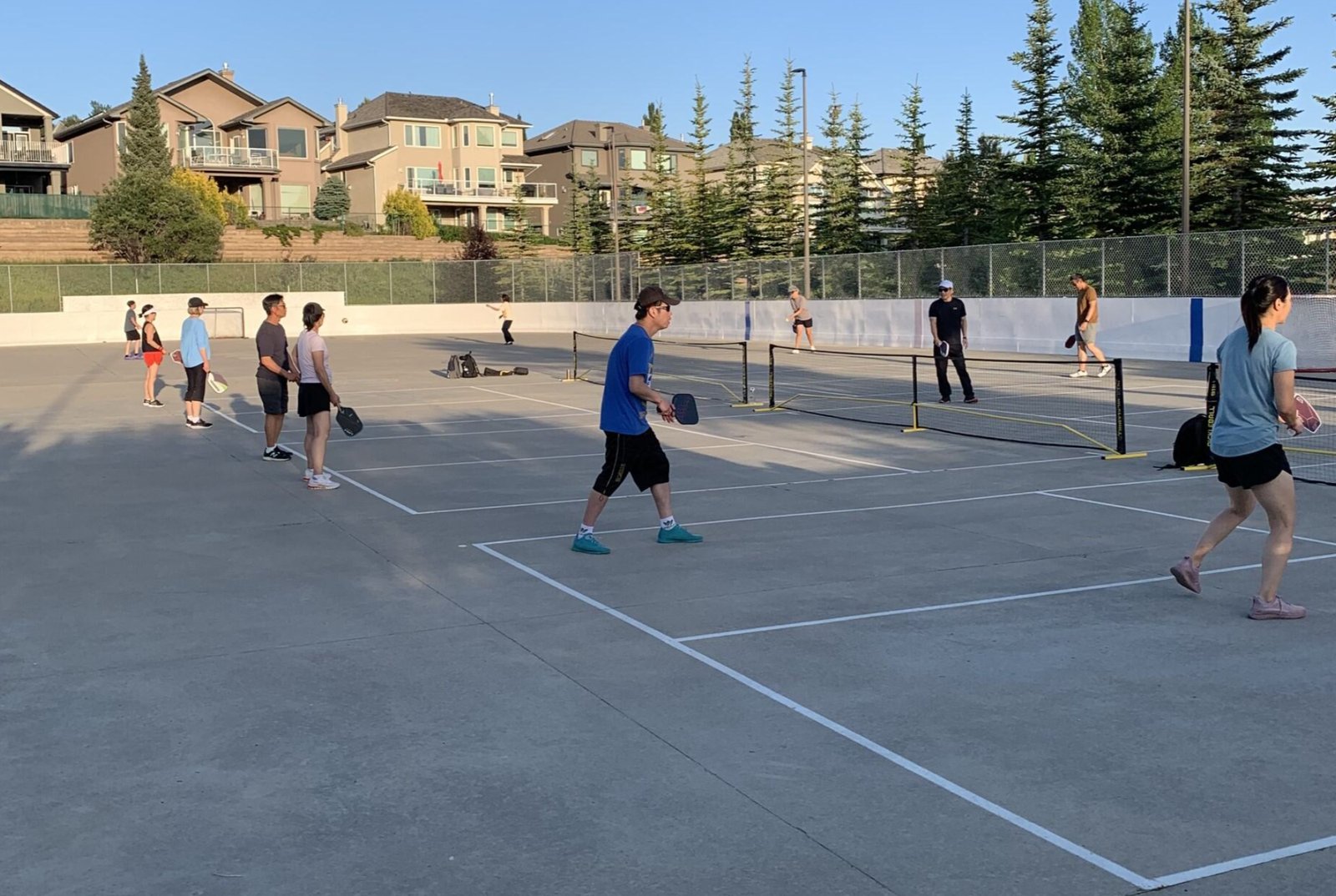 A summer evening on the Signal Hill pickleball courts, players across the painted courts on the rink slab, nets up, paddles in motion.