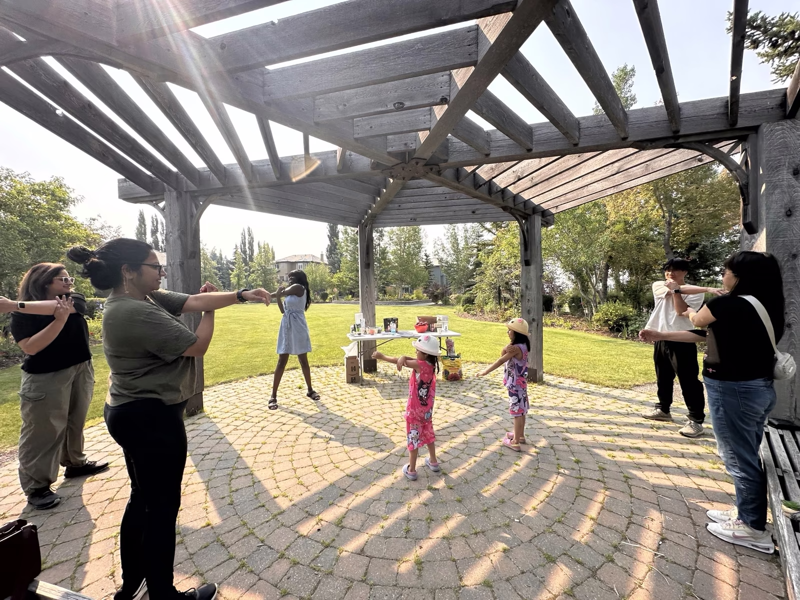 Neighbours of all ages standing in a circle under the gazebo, arms stretched across their chests during the warm-up