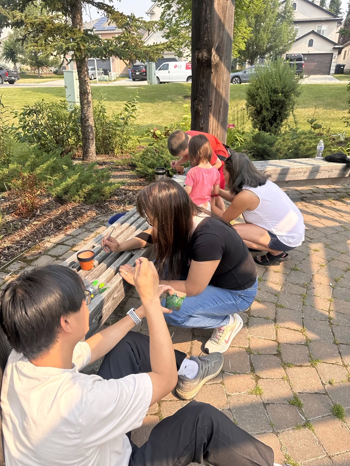 Adults and children painting terracotta pots together along the gazebo benches