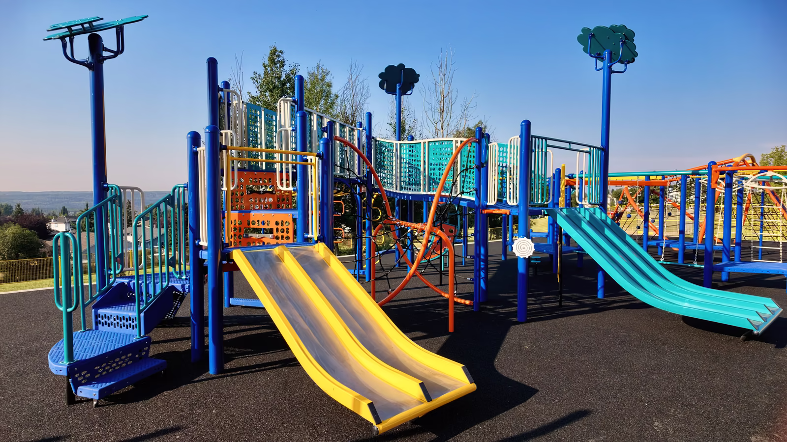 The new playground seen from the field, with a yellow double slide in the foreground and a teal double slide on the right