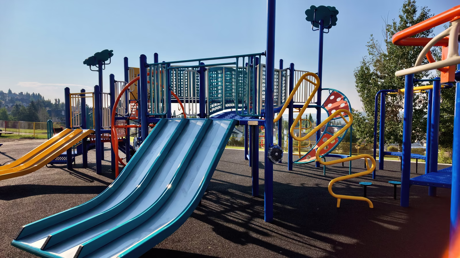 A wide teal double slide beside the main play structure, with a yellow slide visible further along