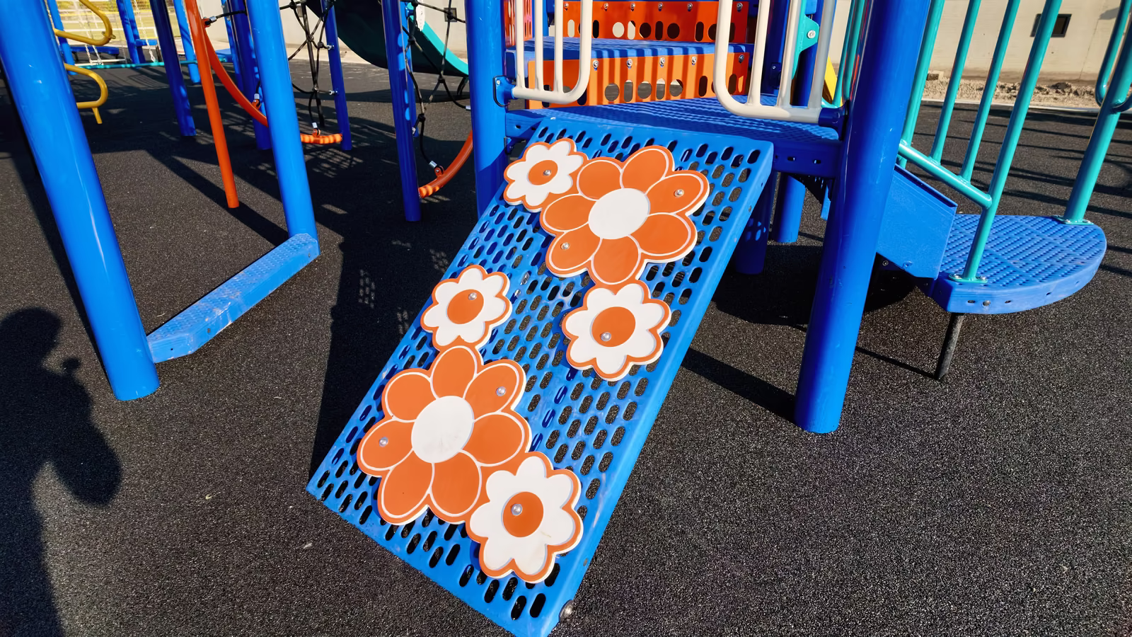 A blue climbing ramp decorated with large orange and white daisy panels