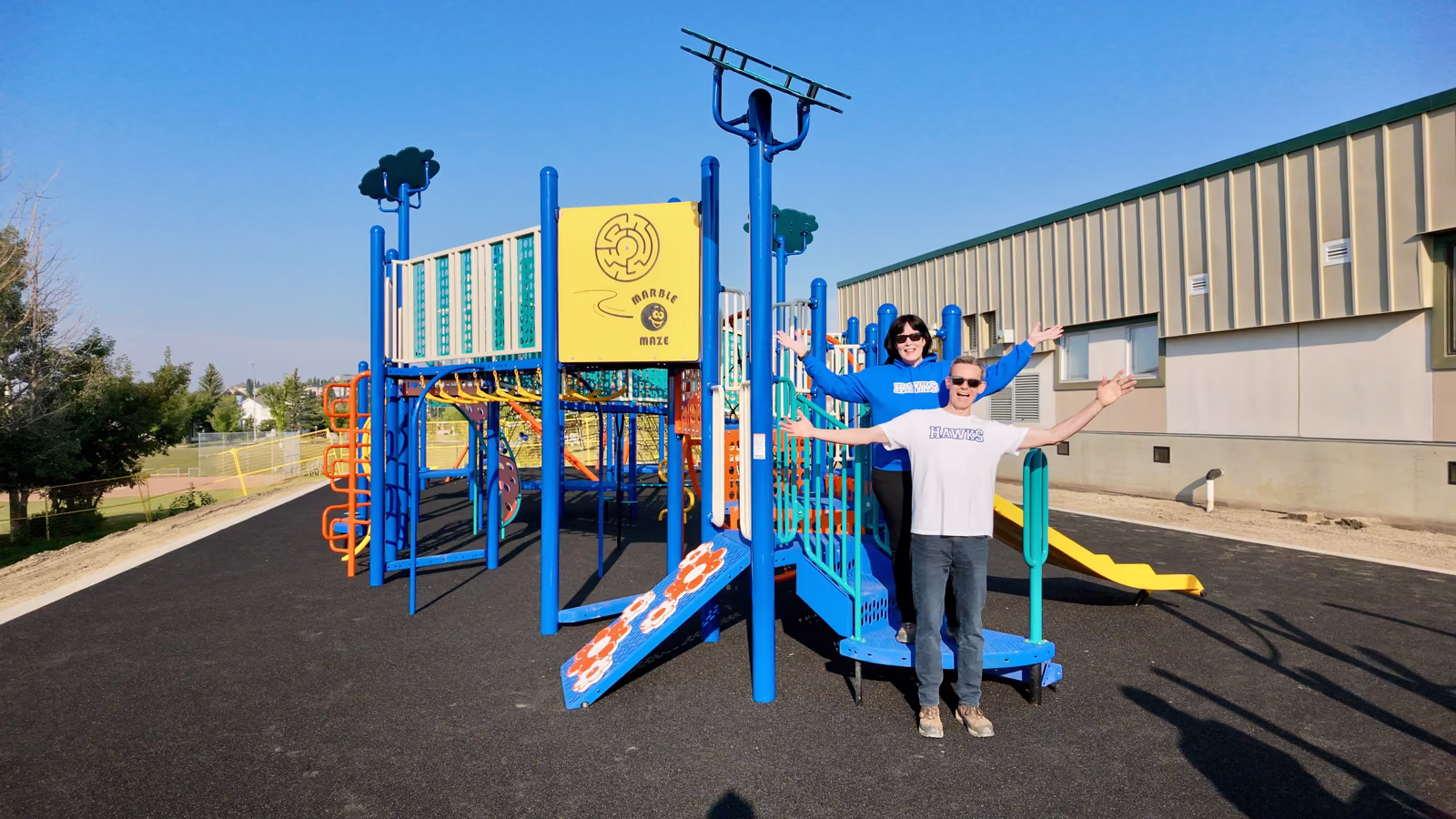 Brian and Kristi McKinnon standing in front of the new playground with their arms out