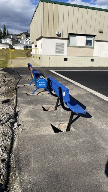 A new blue Buddy Bench beside the school, waiting to be cemented in