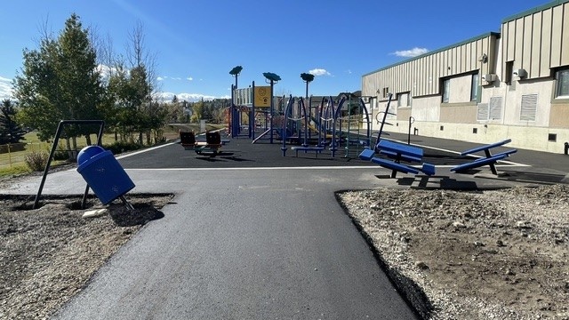 The new Battalion Park School playground with fresh asphalt path, blue benches and play structures, landscaping under way
