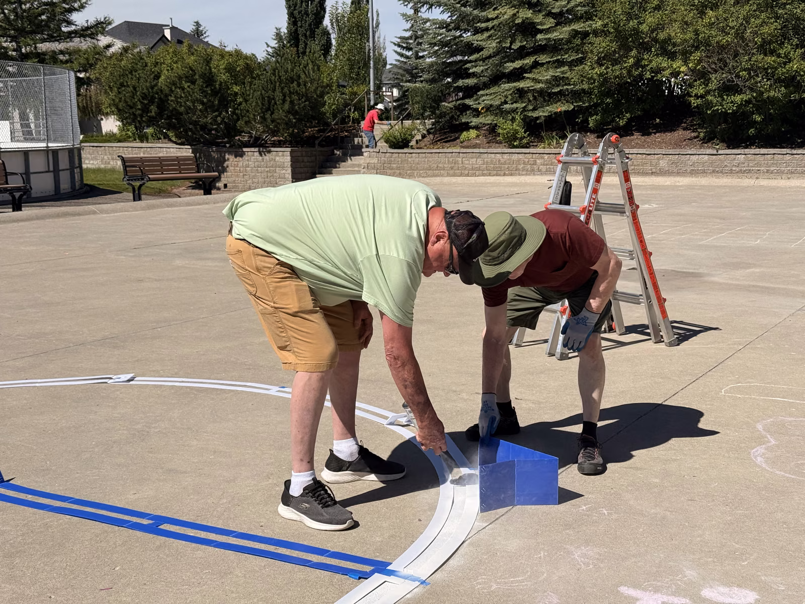 Two volunteers bent over the court, pressing down tape and painting a fresh line